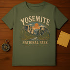 Olive green t-shirt featuring Yosemite National Park vintage graphic with sun, mountains, trees, and water.