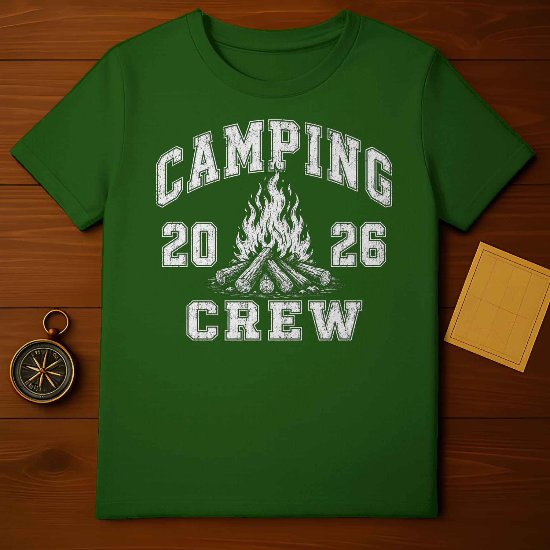Green t-shirt with white distressed text "CAMPING 20 26 CREW" and campfire graphic.