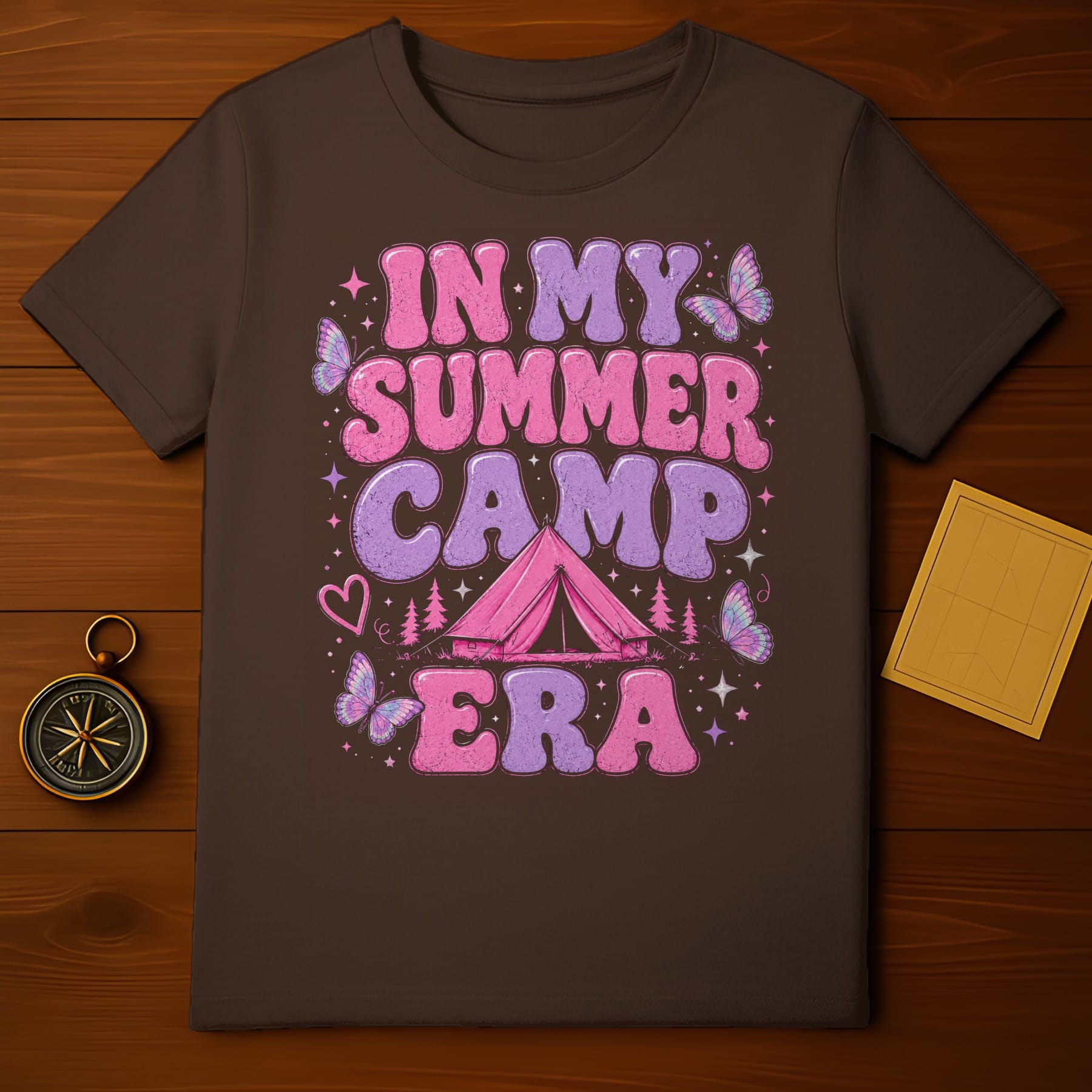 Brown t-shirt with "In My Summer Camp Era" text, tent, pines, hearts, and butterflies.