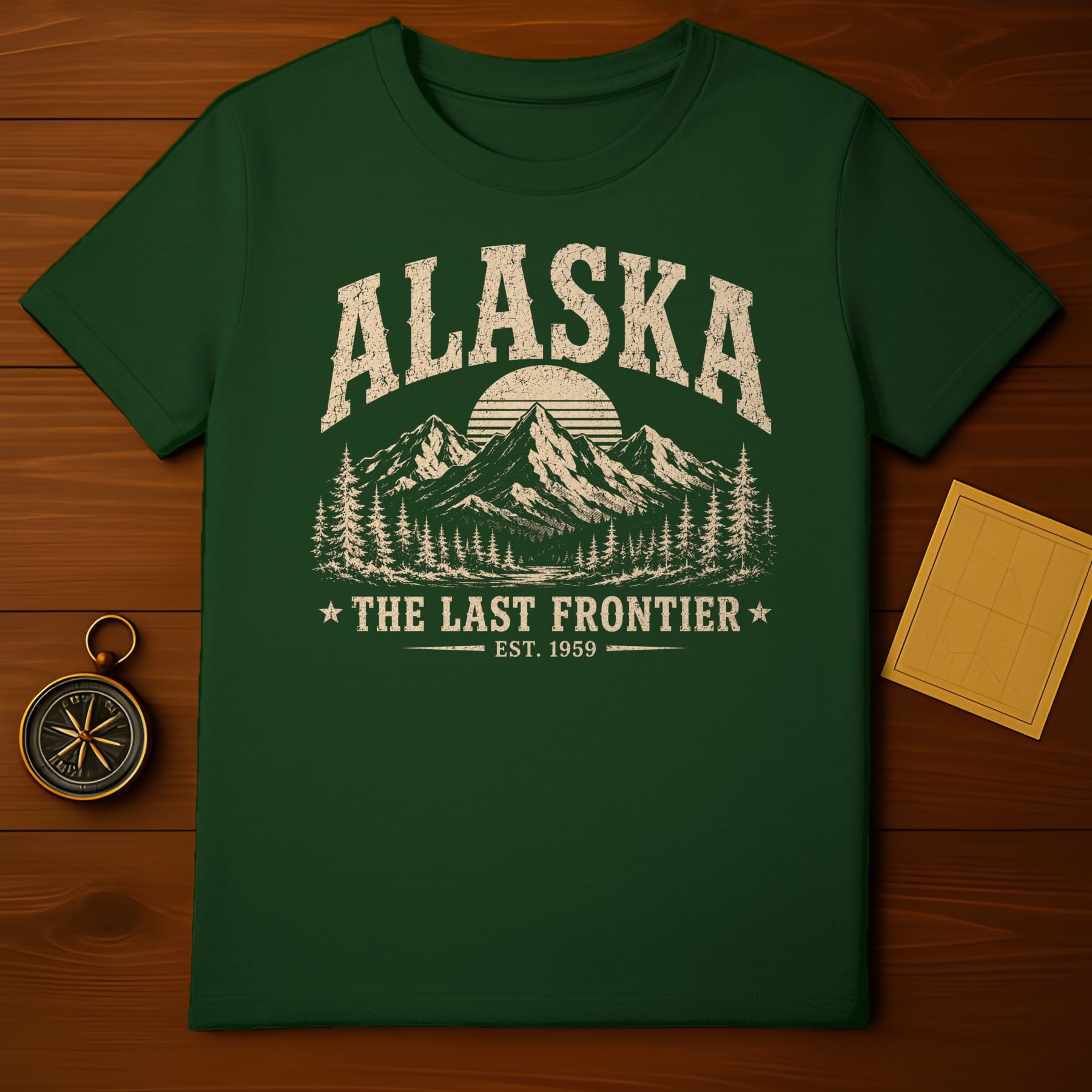 Green t-shirt with "ALASKA," mountains, trees, and "THE LAST FRONTIER EST. 1959" text.