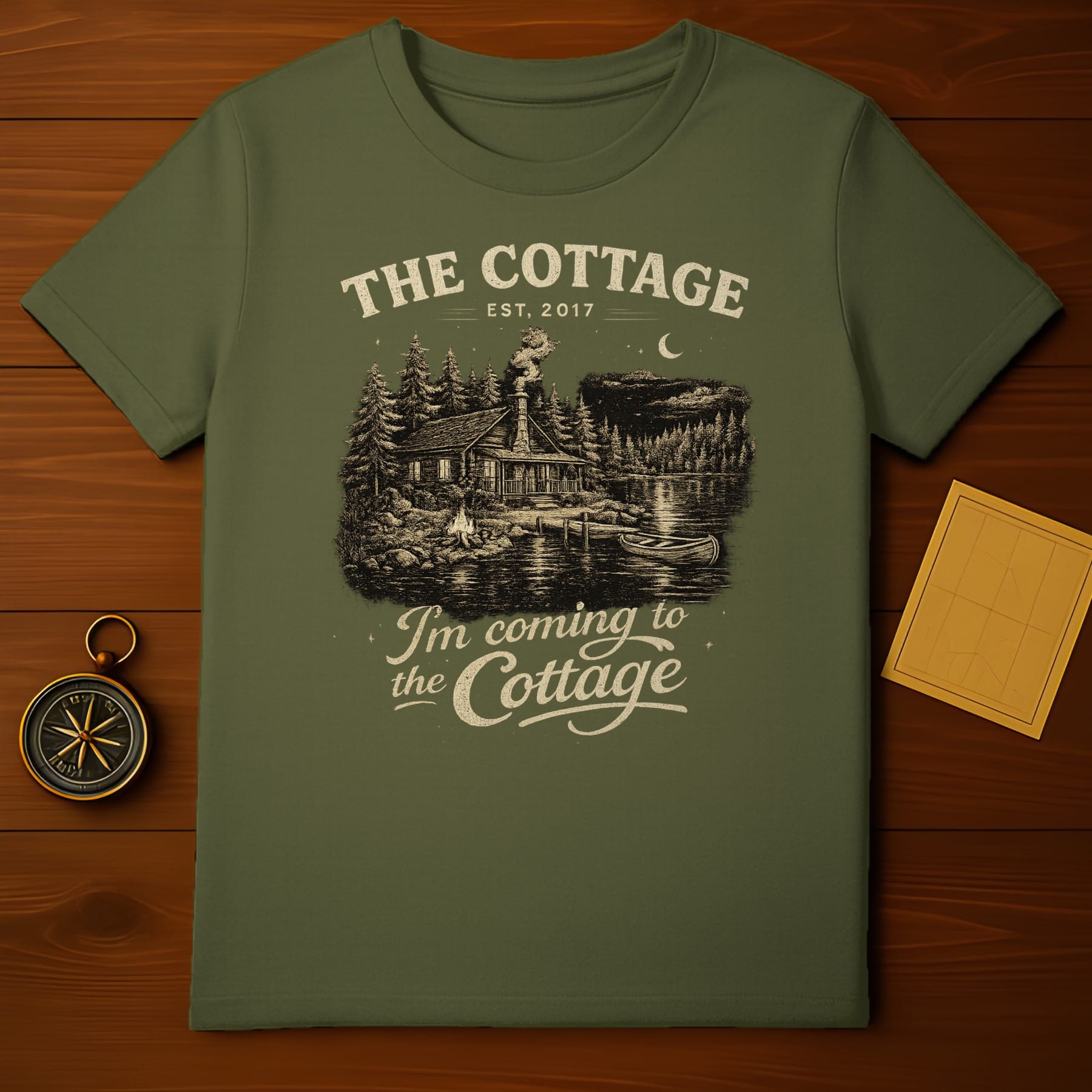 Green t-shirt with "The Cottage" text and a forest cabin scene.