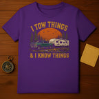 Purplish t-shirt with distressed graphic of truck towing a camper, sunset, and text.