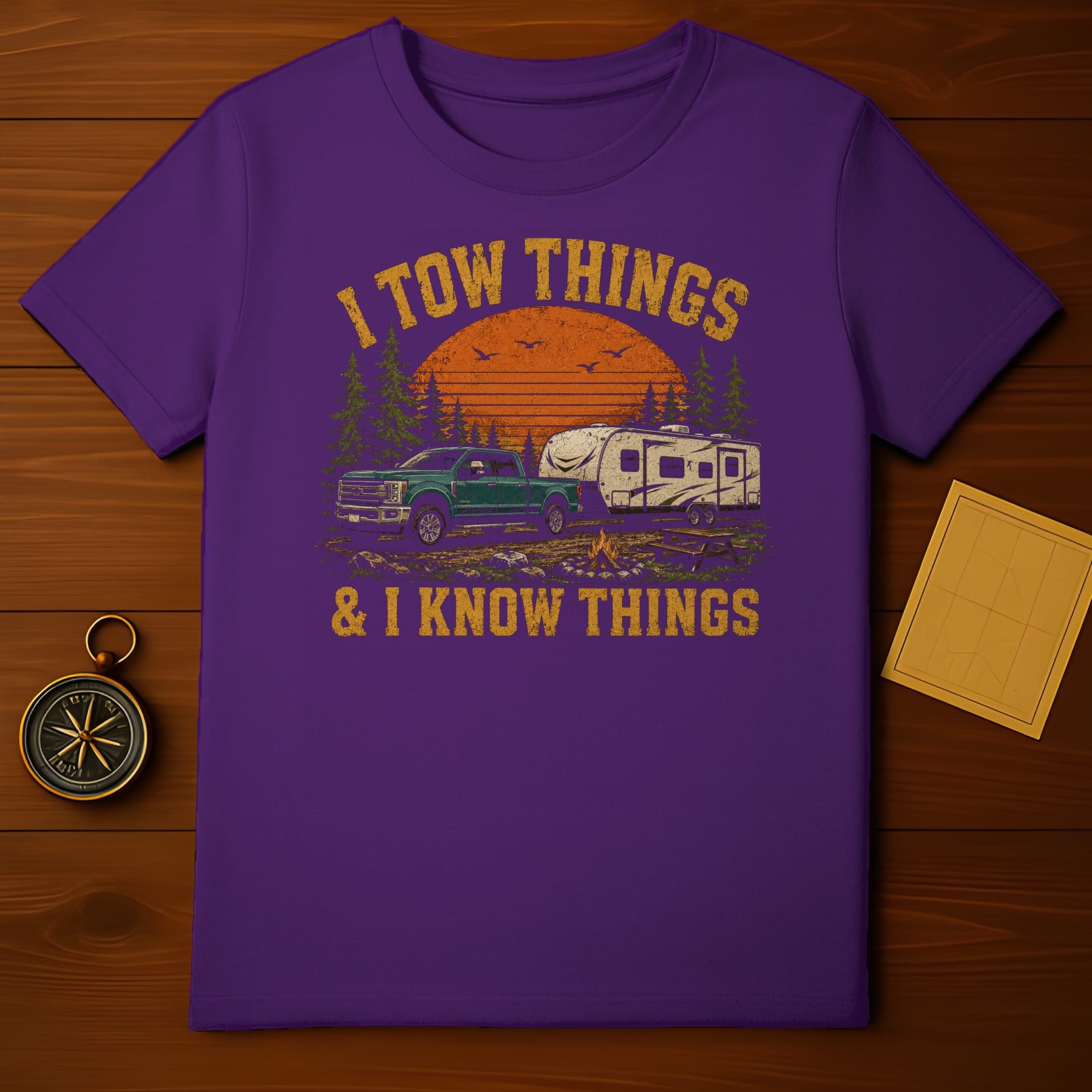 Purplish t-shirt with distressed graphic of truck towing a camper, sunset, and text.