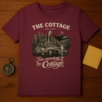 Burgundy t-shirt with "The Cottage" design of a cabin by a lake.