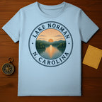 Light blue t-shirt with Lake Norman, N.C. circular graphic featuring a sunset over water.