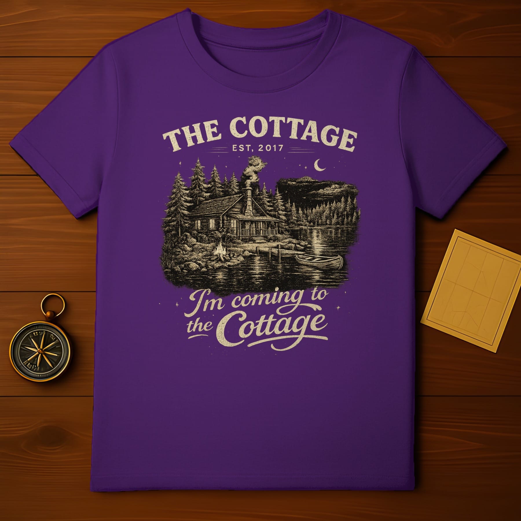 Purple t-shirt with "The Cottage" graphic featuring a log cabin and lake scene.