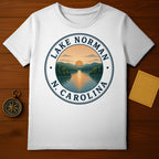 White t-shirt featuring Lake Norman, N.C. circular emblem with sunset over water and mountains.